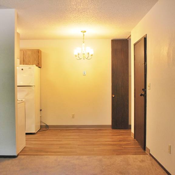 an empty living room with a refrigerator and a door