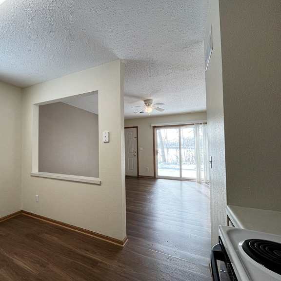 an empty kitchen and living room with wood flooring and a ceiling fan