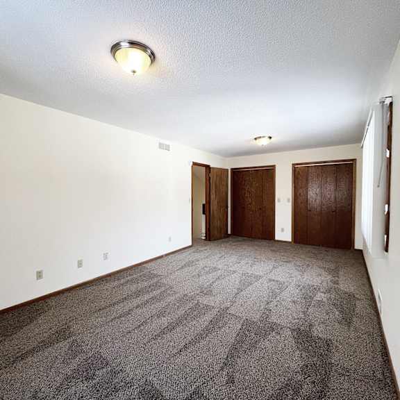 a carpeted room with a white ceiling and two brown doors.