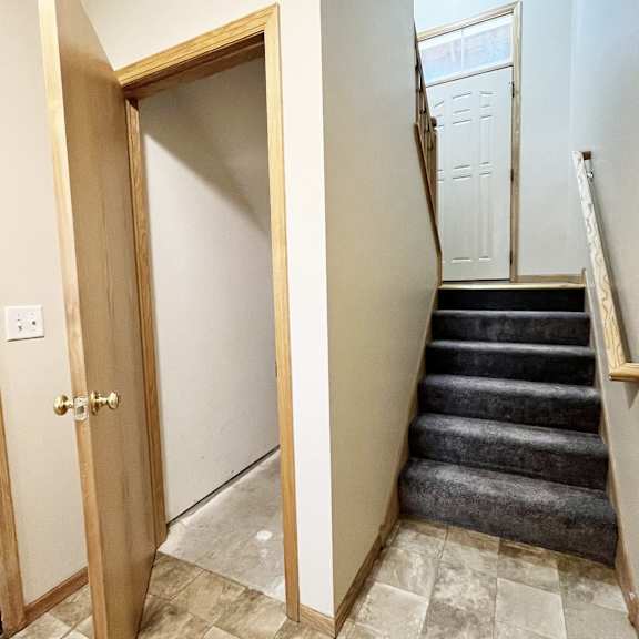 a wooden door is open to a hallway with a staircase.