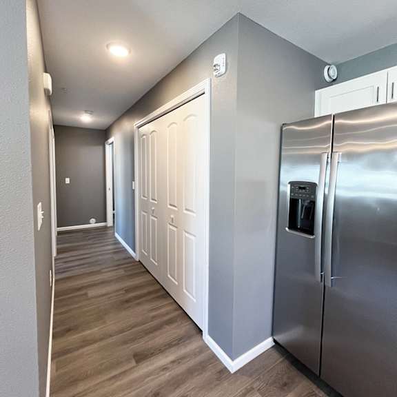 a long hallway with a stainless steel refrigerator on the right.