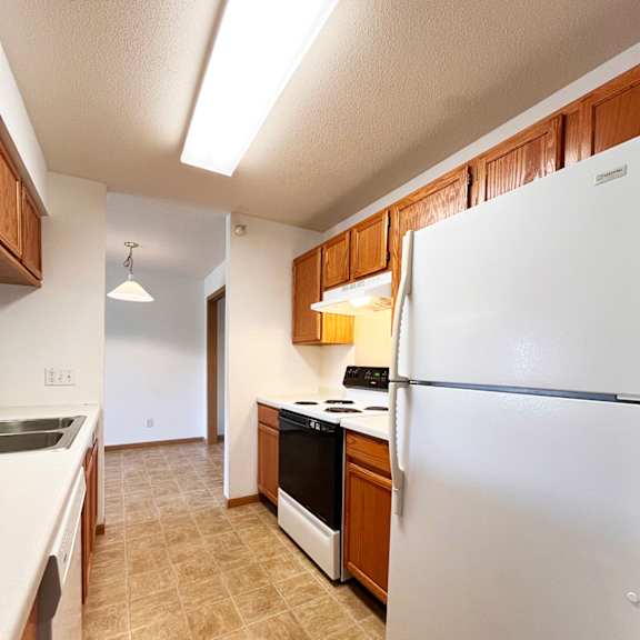 a kitchen with a white refrigerator, brown cabinets, and a tiled floor.