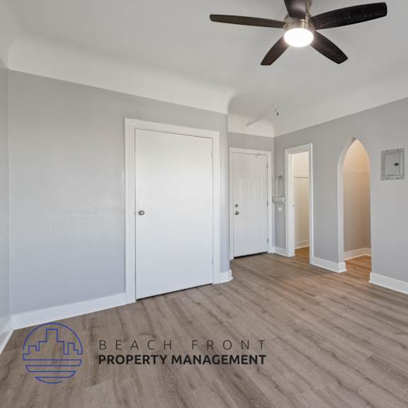 a renovated living room with a ceiling fan and a hallway to two closets