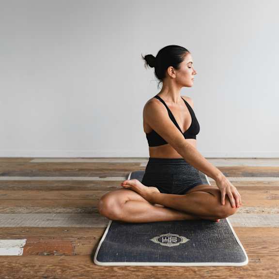 A woman is sitting on a yoga mat in a meditative pose.