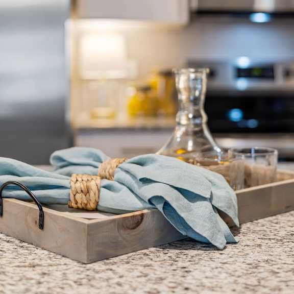 A wooden tray with a cloth and a bottle on a kitchen counter.