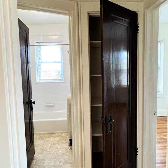 a closet in a bedroom with a door open to a bathroom with a tub and a window