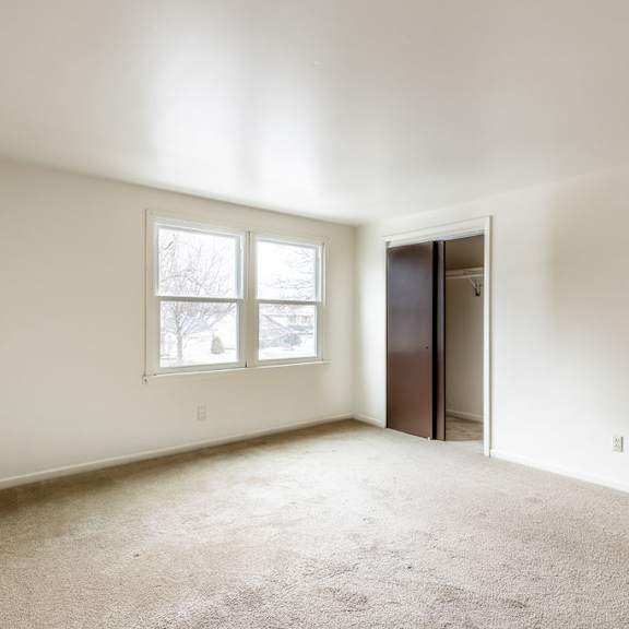 a room with a carpeted floor, a window, and a door.