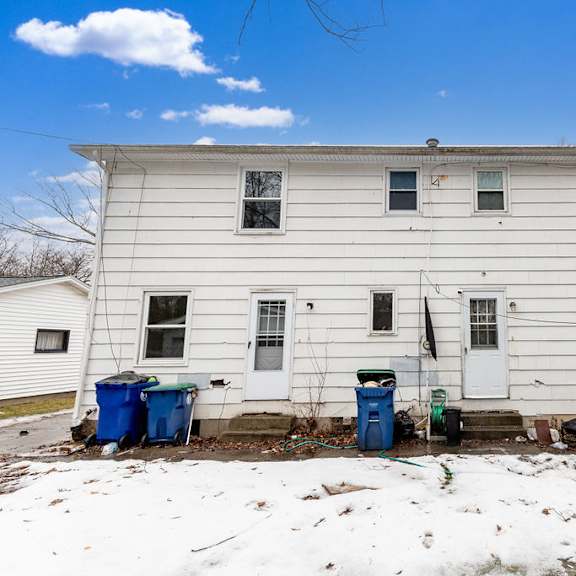 a white house with a broken window and trash bins in front.