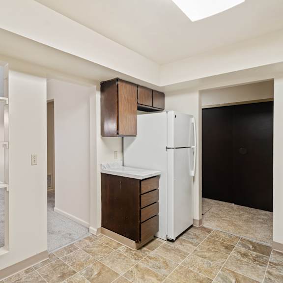 a kitchen area with a white refrigerator and brown cabinets.
