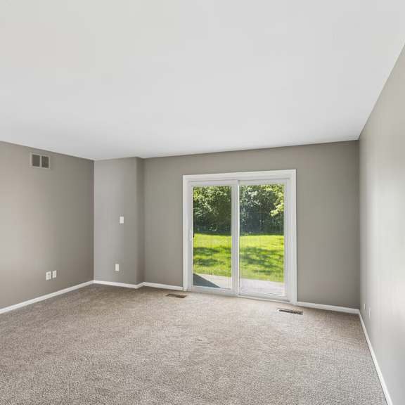 a room with a carpeted floor and a sliding glass door leading to a green outdoor area.