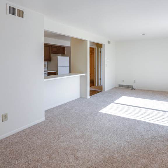 an empty living room with a kitchen in the background