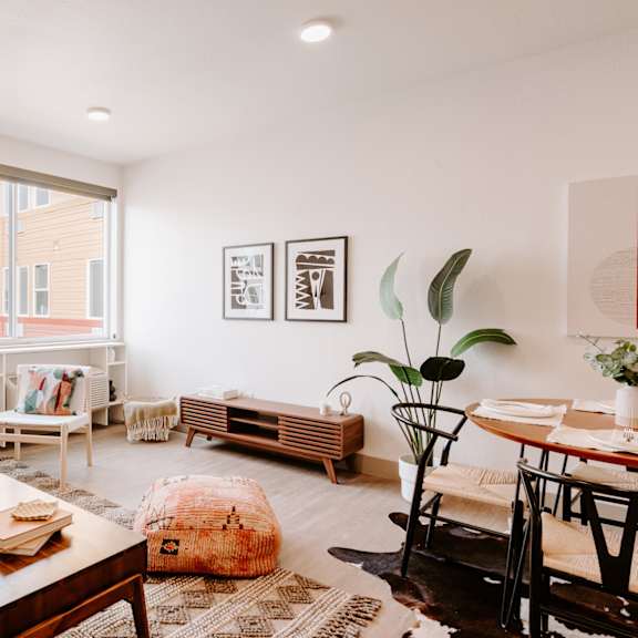 a living room with a brown leather couch, a wooden coffee table, and a large window with a view of a building outside.