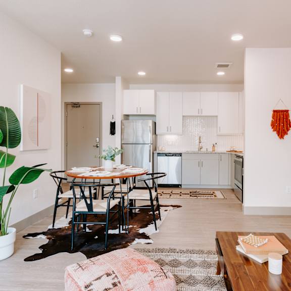 a living room with a dining table and chairs, a couch, and a potted plant.