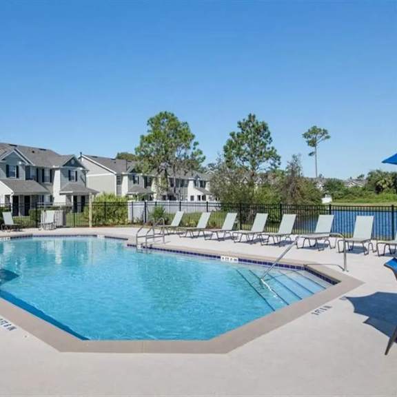 a resort style pool with chaise lounge chairs and apartment buildings in the background