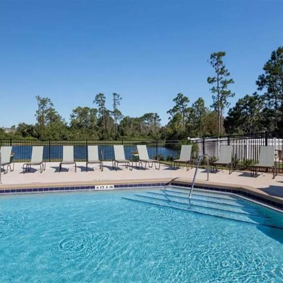 a swimming pool with chaise lounge chairs and trees in the background