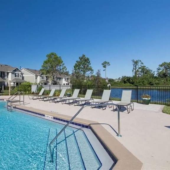 a swimming pool with chaise lounge chairs in front of a row of houses