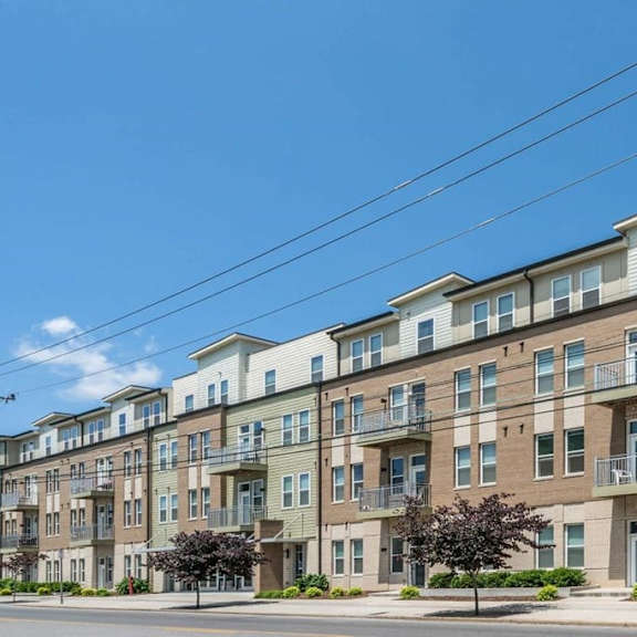 A row of apartment buildings with balconies and trees in front.