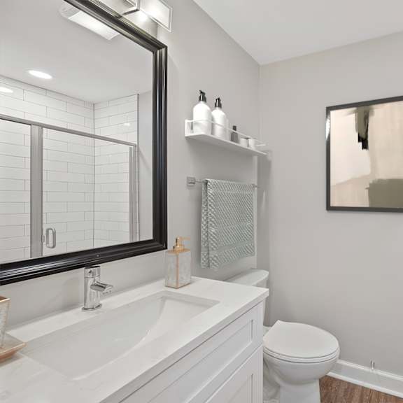 Thumbnail 14 of 18 A white bathroom with a toilet, sink, mirror, and a picture on the wall. at Indian Creek Apartments*, Cincinnati, OH