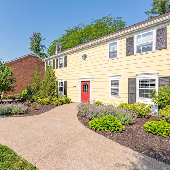 Thumbnail 21 of 25 A yellow house with a red door is surrounded by greenery and a concrete pathway. at Indian Creek Apartments*, Ohio