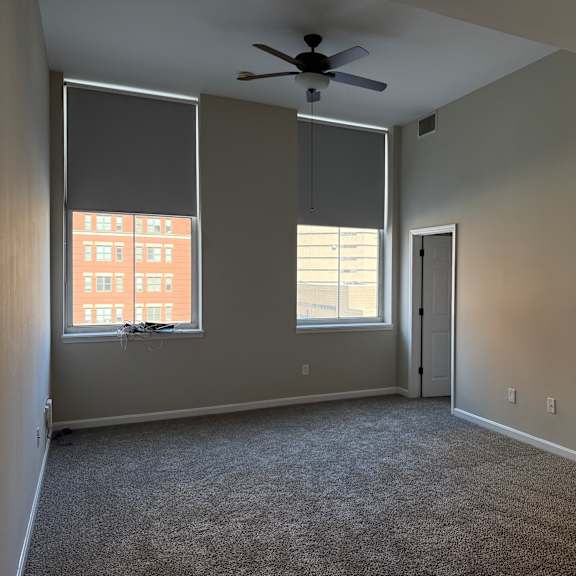 Thumbnail 4 of 10 A room with a ceiling fan and two windows.