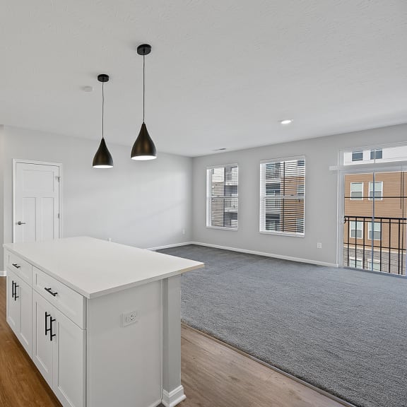 Thumbnail 7 of 19 an open kitchen and living room with white cabinets and a white island with two lights at Monmouth Row Apartments, Newport, Kentucky
