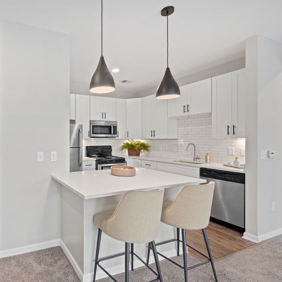 Thumbnail 5 of 15 a kitchen with white cabinets and a white island with two stools at Monmouth Row Apartments, Newport, Kentucky
