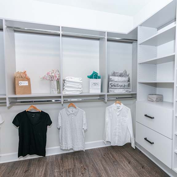 Thumbnail 5 of 8 A white closet with clothes hanging and shelves.