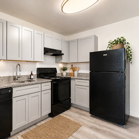 a black refrigerator stands in a kitchen with white cabinets and a black dishwasher.