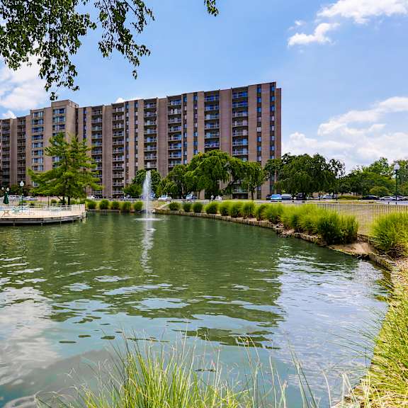 a large building is situated next to a body of water with a fountain in the middle.