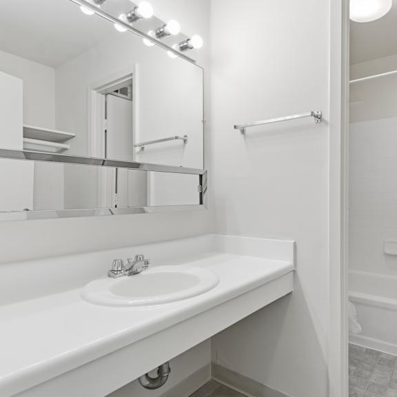 a white bathroom with a sink, mirror, and bathtub.