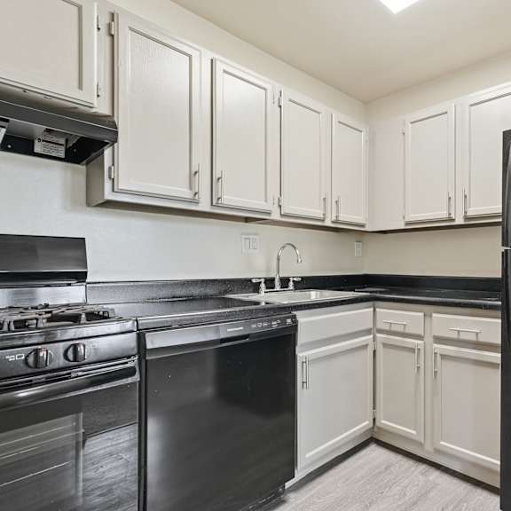 a black refrigerator stands in a kitchen with white cabinets.