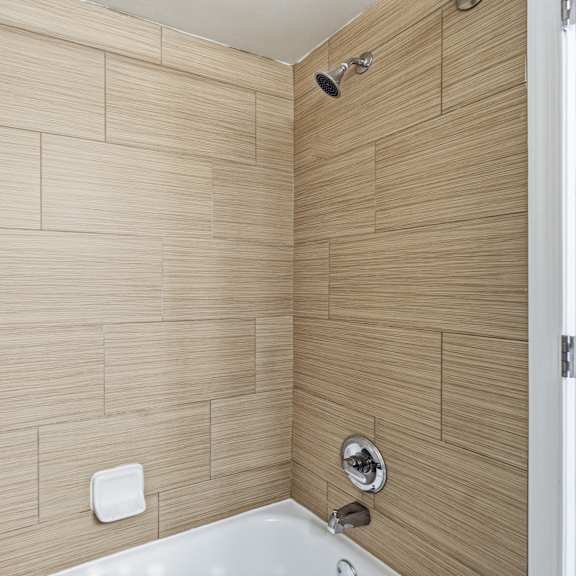 a white bathtub sits in a bathroom with tan tiled walls.