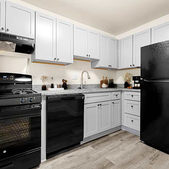 a black refrigerator sits in a kitchen with white cabinets at seven springs apartments, college park