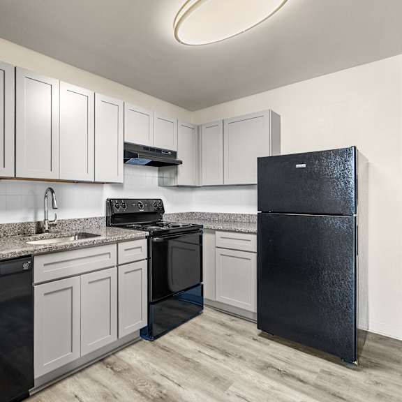 a black refrigerator stands in a kitchen with white cabinets and a black stove.