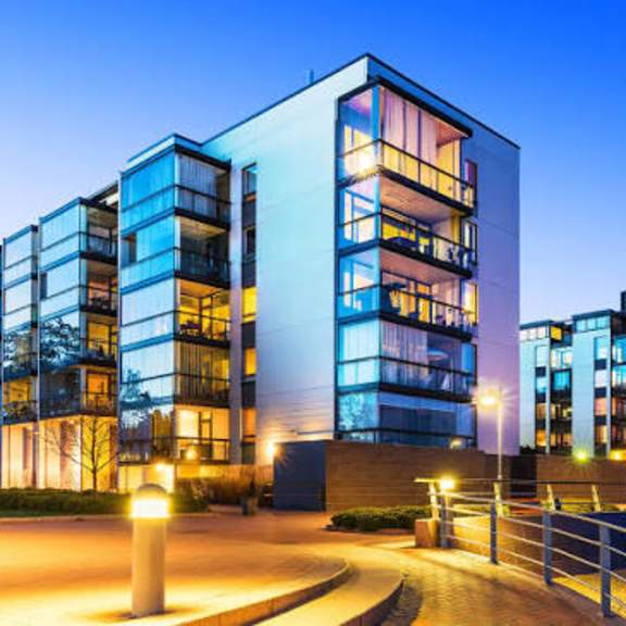 a modern building with glass windows and balconies is illuminated at dusk.