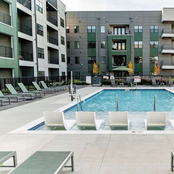 a swimming pool surrounded by white chairs and loungers in front of a building at harbor side at conwood flats apartments in uptown memphis, tn