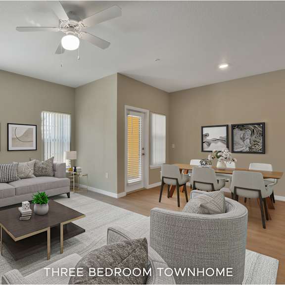 a well-lit, spacious living room with a grey sofa, a coffee table, and a dining area with a table and chairs.