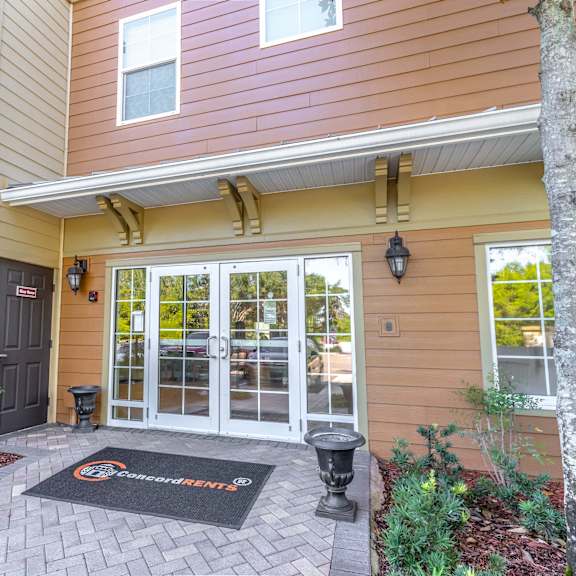 the entrance to a building with glass doors and a welcome mat in front of it