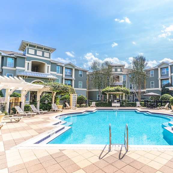 a swimming pool with lounge chairs and umbrellas in front of an apartment building