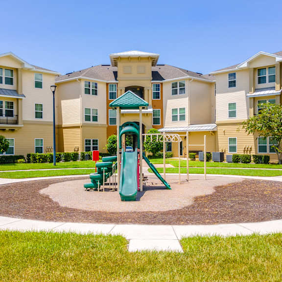 a playground area with a green slide is surrounded by apartment buildings.