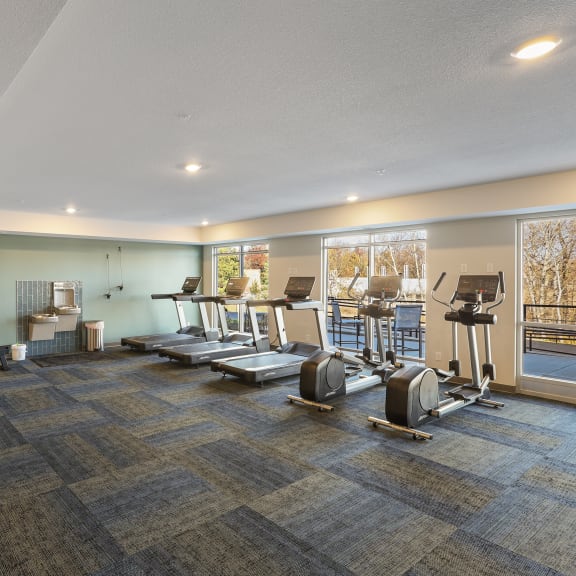 a gym with treadmills and other exercise equipment in a building with windows