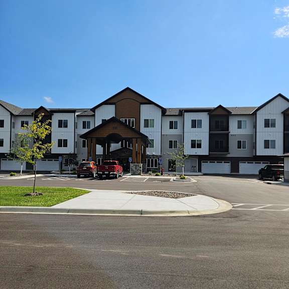 a large white building with a brown roof and a parking lot in front.