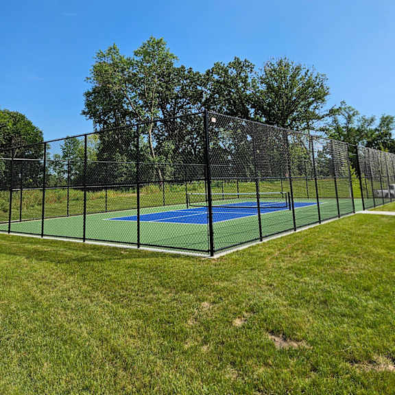 a tennis court is surrounded by a green fence and trees.