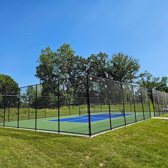 a tennis court enclosed by a black fence with trees in the background.