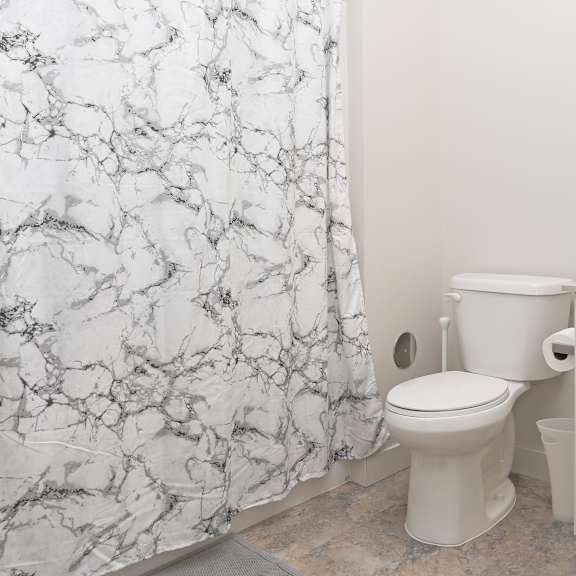 a white toilet sits in a bathroom with a marble shower curtain.