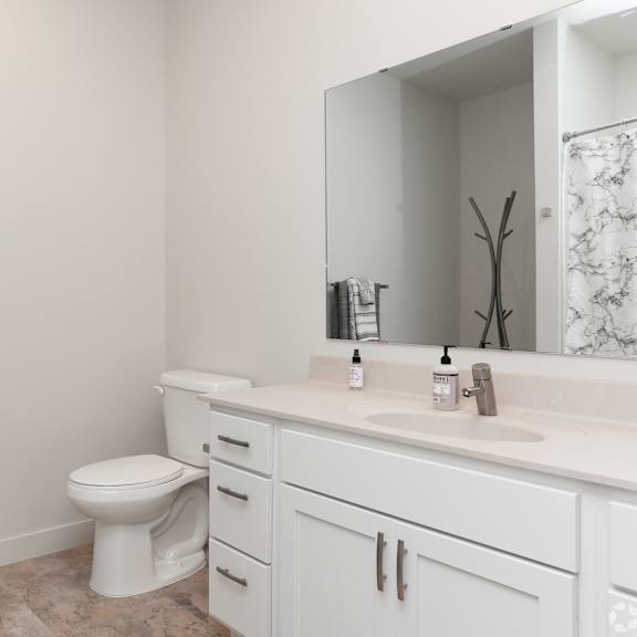 a white bathroom with a toilet, sink, and mirror.
