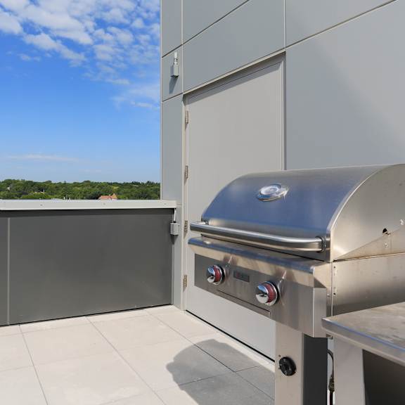 a silver barbecue grill on a patio with a view of trees and sky.