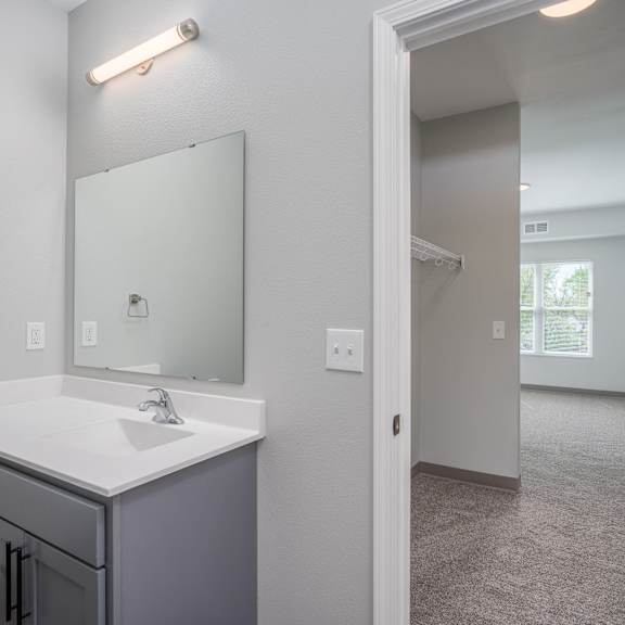 an empty bathroom with a sink and mirror and a walk in closet
