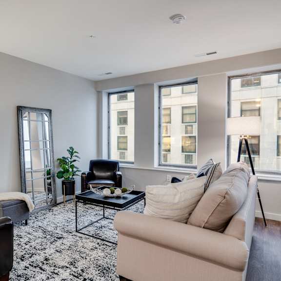 a living room with a black chair, a beige couch, and a black and white rug.