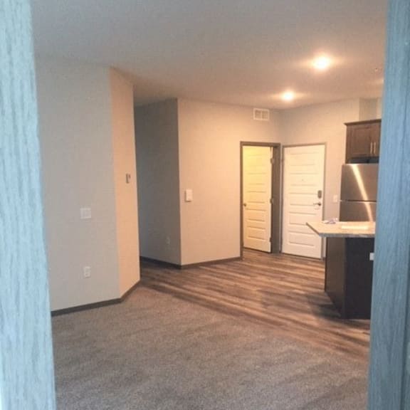 an empty living room with a kitchen and a door